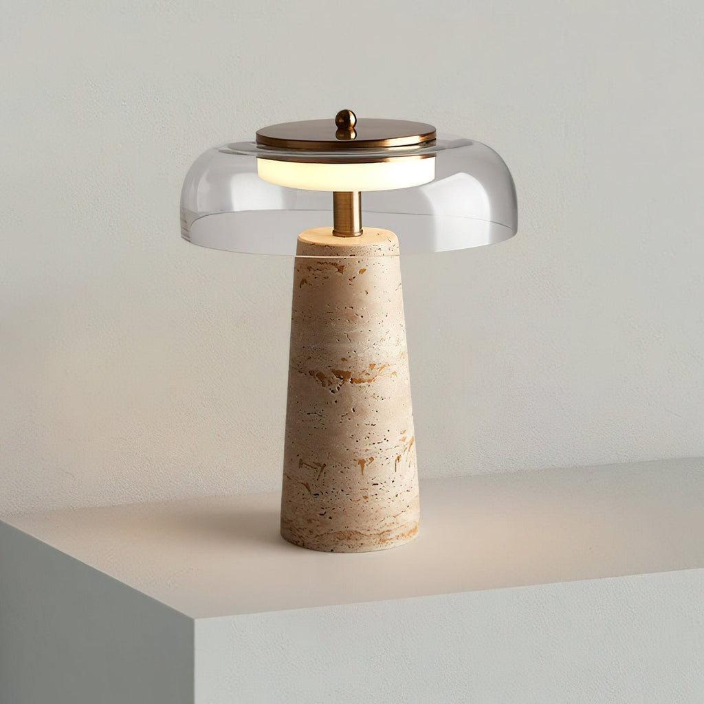 Clear glass dome with a brass cap on this Clérachic table lamp, its travertine base resting on a pale stepped plinth.