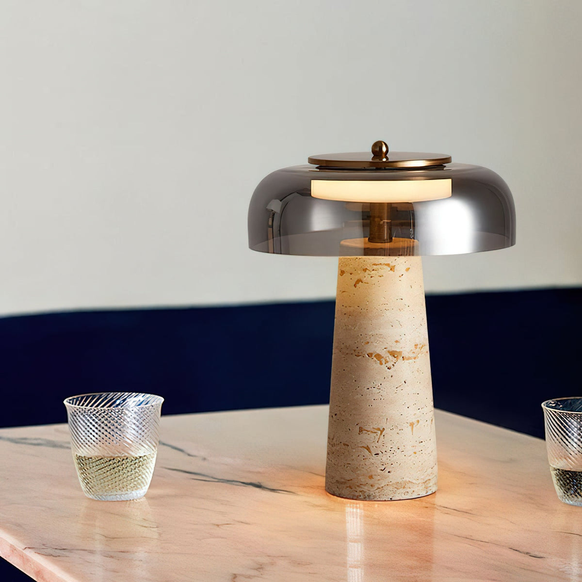 Smoky grey dome and veined travertine base on a pink-veined marble table, with two ribbed glasses of white wine beside this Clérachic lamp.