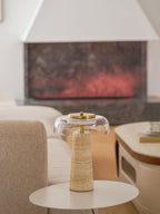 Wider view of this Clérachic lamp on a round white side table, with a stone fireplace and a pale sofa in the background.