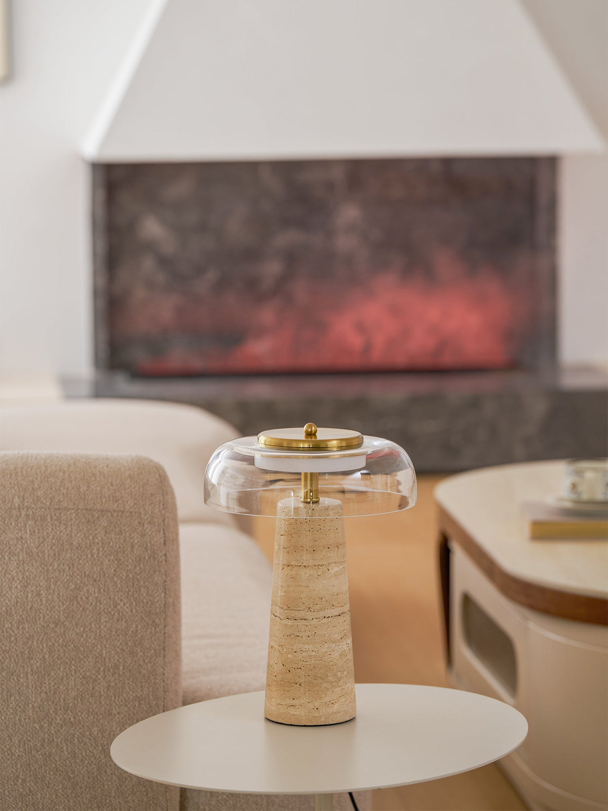 Wider view of this Clérachic lamp on a round white side table, with a stone fireplace and a pale sofa in the background.