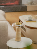 Portrait view of this Clérachic table lamp, unlit, on a round white table beside a cream sofa and an oval coffee table with a teacup.