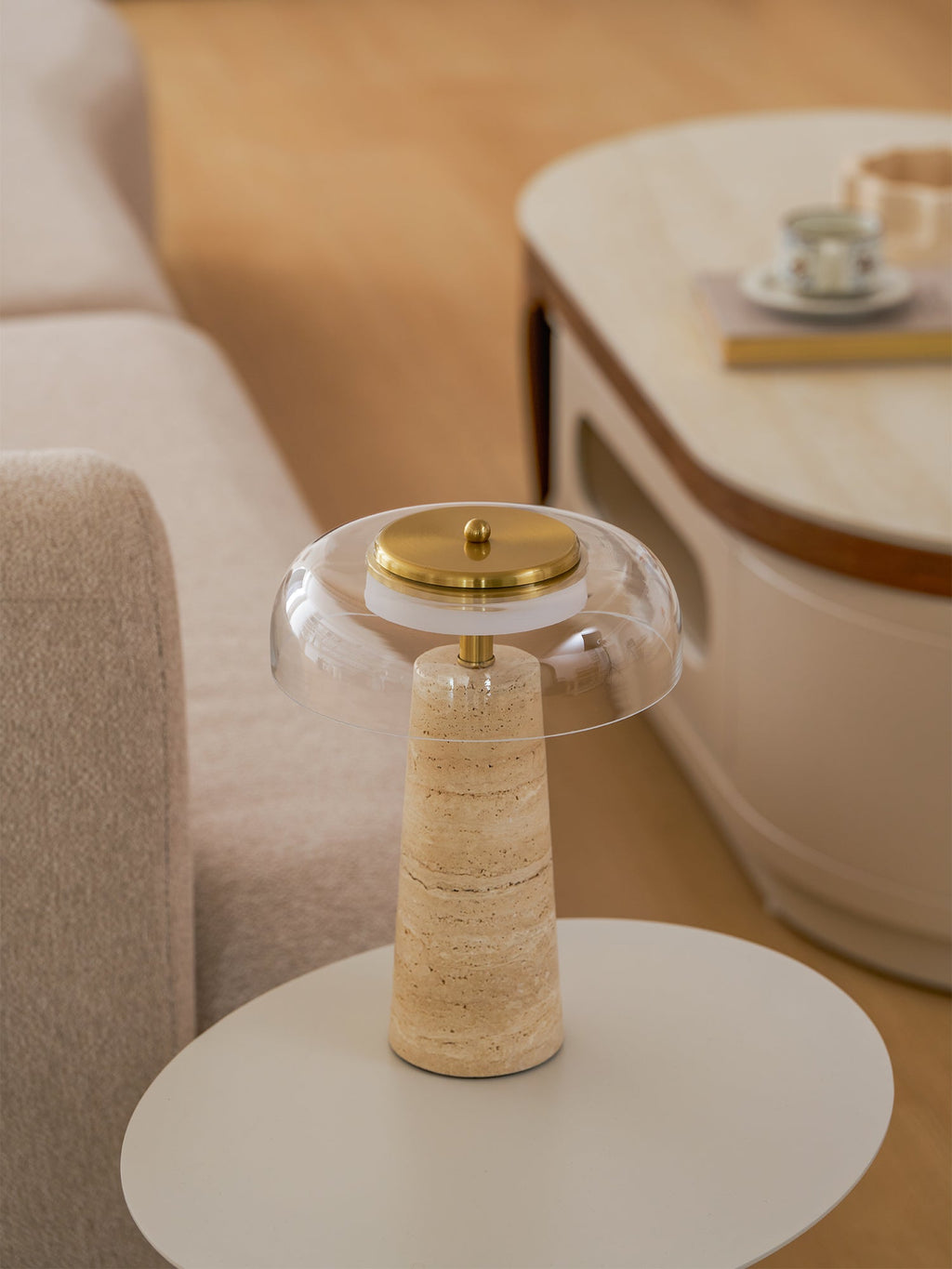 Close framing of the clear glass dome and brass cap on this Clérachic lamp, set on a round white table by a sofa.