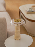 Close framing of the clear glass dome and brass cap on this Clérachic lamp, set on a round white table by a sofa.