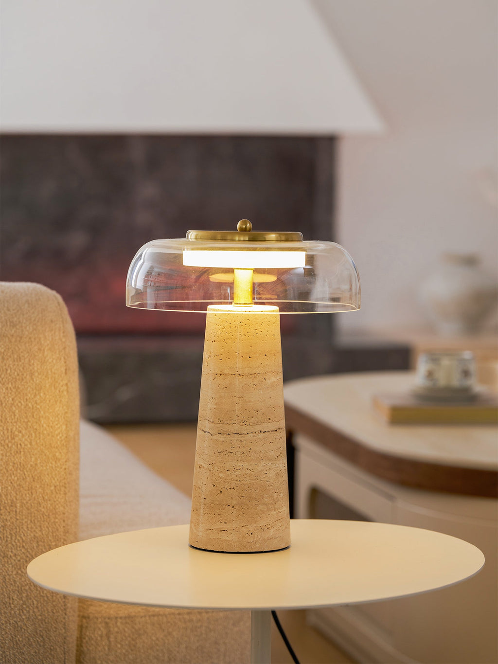 Evening glow from this Clérachic table lamp, its clear dome lit and the beige travertine base warmed by the light.
