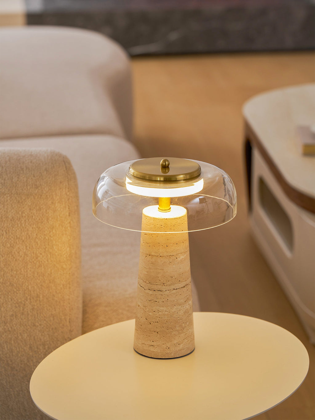 Close view of the lit clear dome on this Clérachic lamp, with the pale round table and cream sofa softly blurred behind.