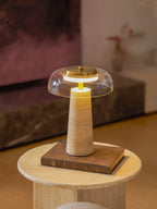 Clérachic table lamp lit on a stack with a book, set against a dark stone fireplace and a warm wooden floor.