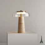 This Clérachic table lamp lit on a white plinth against a grey wall, with a small Eiffel Tower figurine at the right edge.