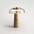 Studio shot of a clear-dome Clérachic table lamp, softly lit on a pale grey surface with a brass cap and finial.