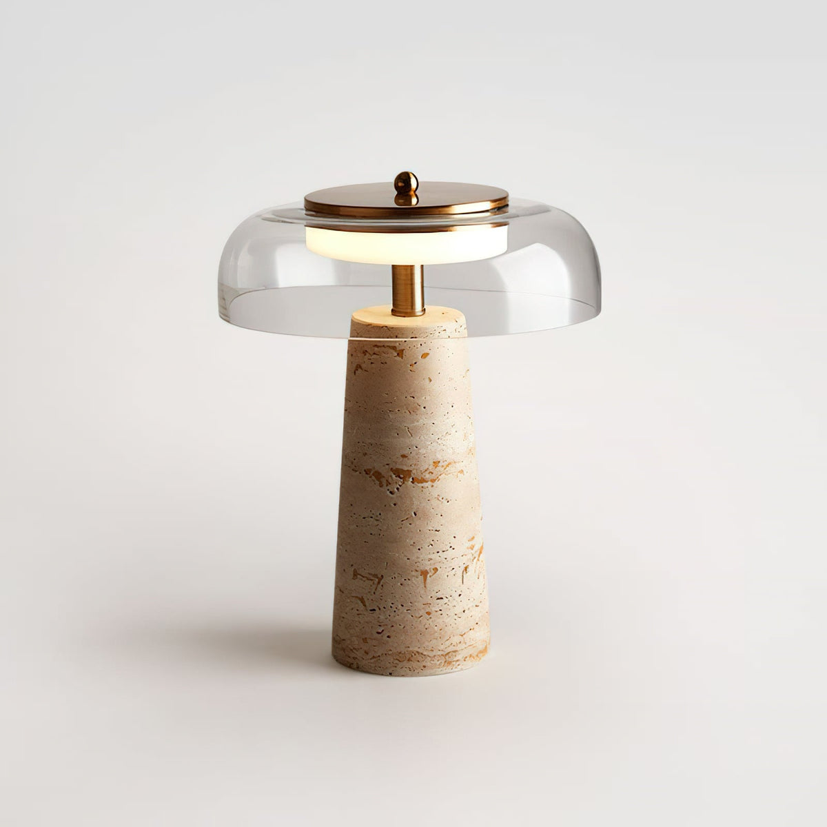 Studio shot of a clear-dome Clérachic table lamp, softly lit on a pale grey surface with a brass cap and finial.