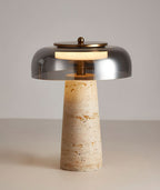 Smoky grey dome lit above a tapering travertine base, this Clérachic table lamp is shown on a pale grey tabletop.
