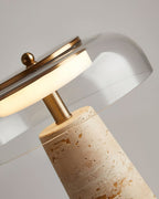 Angled close view of the brass stem and clear glass dome on this Clérachic table lamp, where the travertine base meets the stem.
