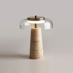 Clear-dome Clérachic table lamp lit on a pale tabletop, with the dome's rim and brass cap catching the soft studio light.
