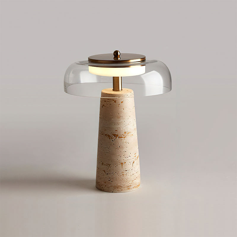 Clear-dome Clérachic table lamp lit on a pale tabletop, with the dome's rim and brass cap catching the soft studio light.