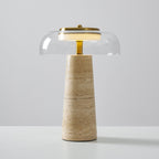 Clérachic table lamp with a clear glass dome and brass stem, its banded beige travertine base standing on a white surface.