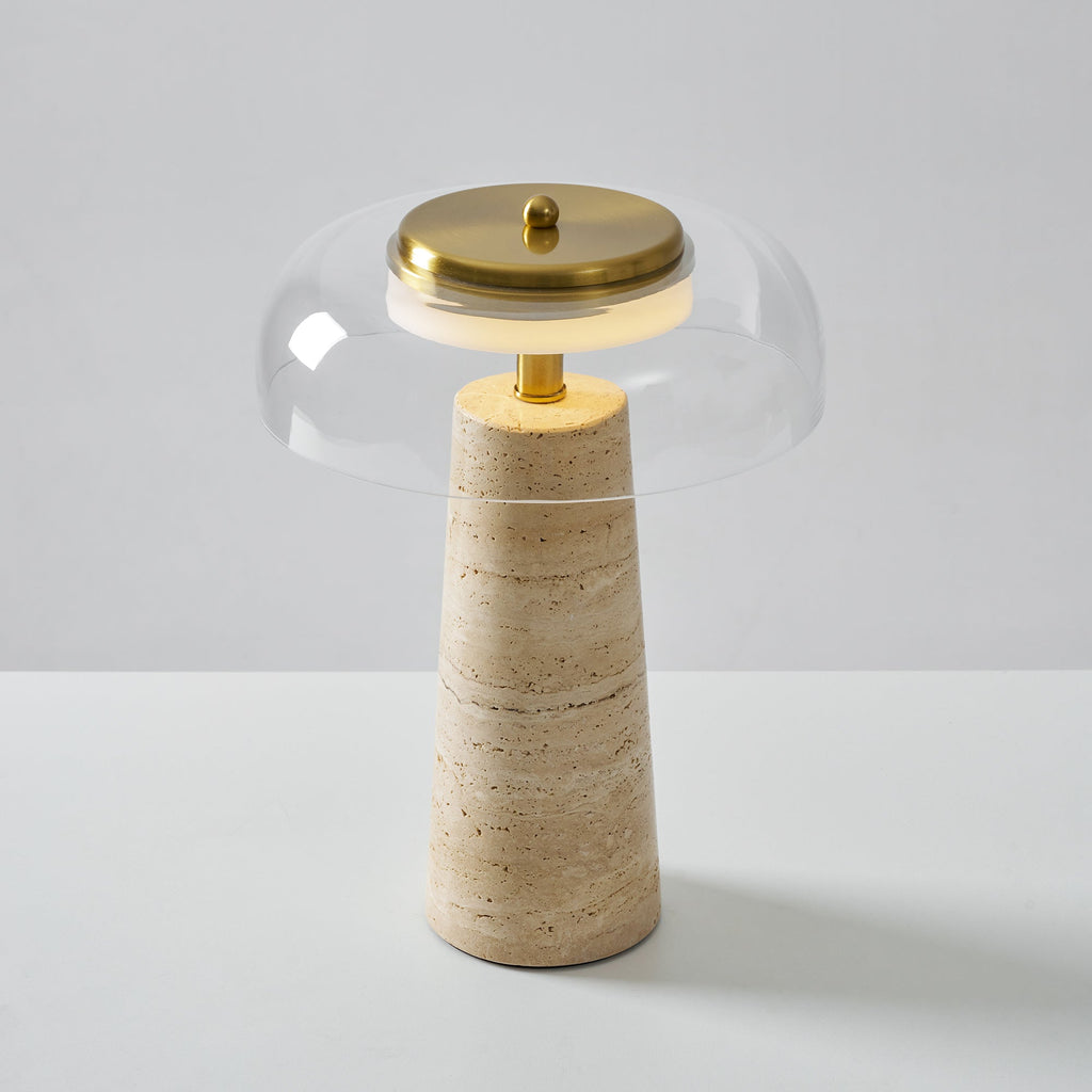Clérachic travertine table lamp seen from slightly above, the glass dome glowing over a brass cap and a softly banded base.