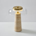 Clérachic travertine table lamp seen from slightly above, the glass dome glowing over a brass cap and a softly banded base.