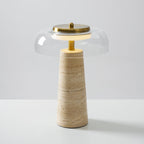 The brass stem and a glowing ring beneath a clear glass dome on this Clérachic table lamp, with a banded travertine base.