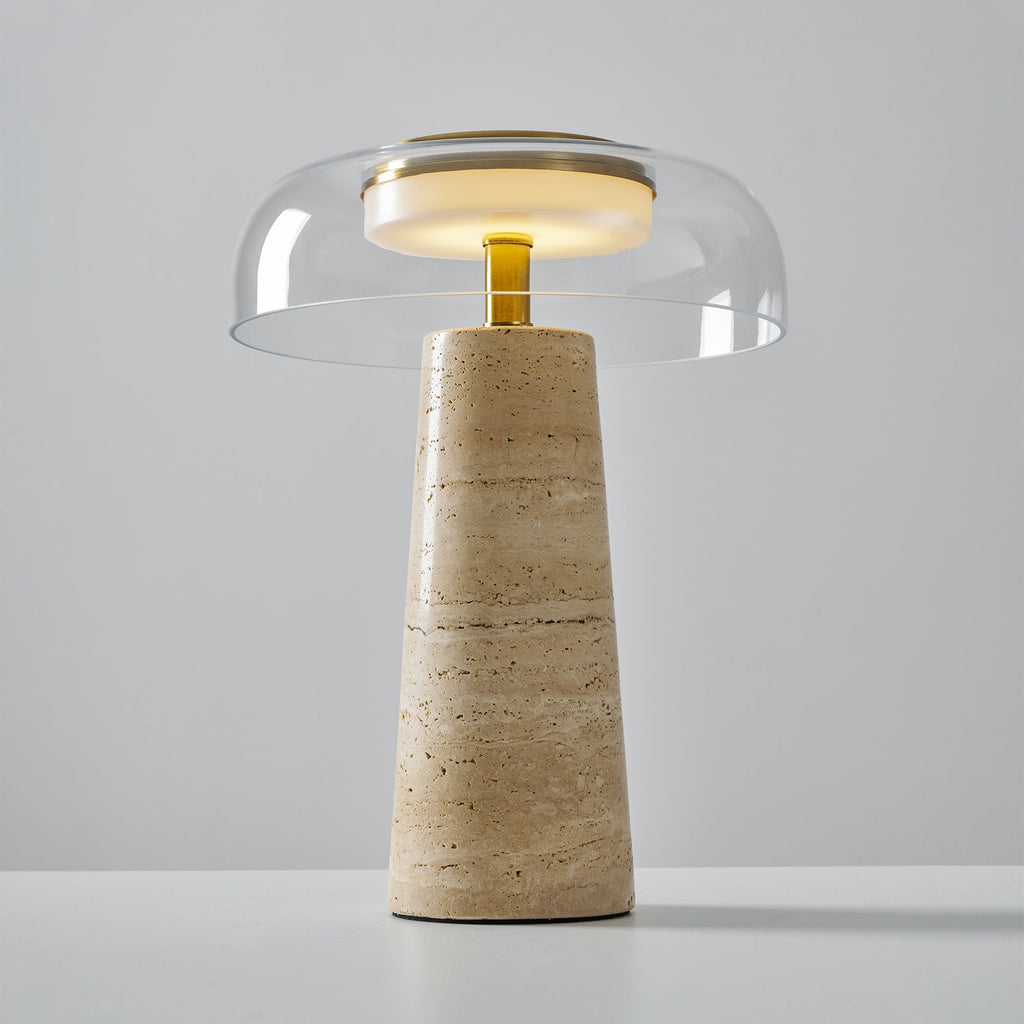 A lit clear dome sits above a brass stem on this Clérachic table lamp, its base showing fine horizontal travertine bands.