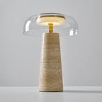 A lit clear dome sits above a brass stem on this Clérachic table lamp, its base showing fine horizontal travertine bands.