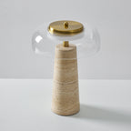 Slightly higher view of this Clérachic table lamp, a brass cap crowning a clear glass dome above the travertine base.