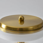 Close view of the brass cap and ball finial on top of this Clérachic table lamp, above the glowing ring beneath the dome.