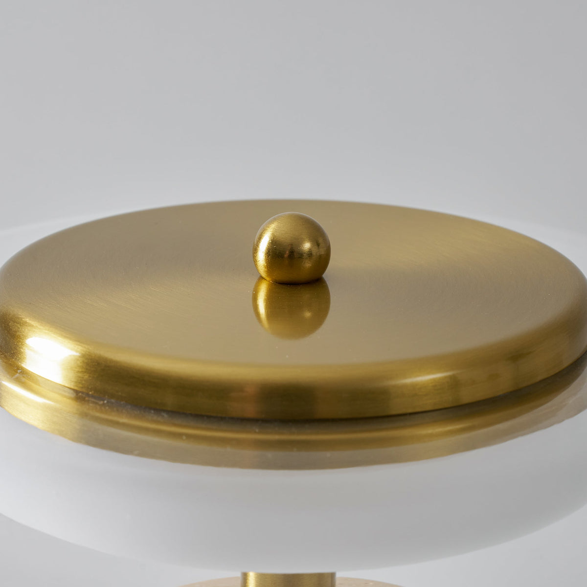 Close view of the brass cap and ball finial on top of this Clérachic table lamp, above the glowing ring beneath the dome.