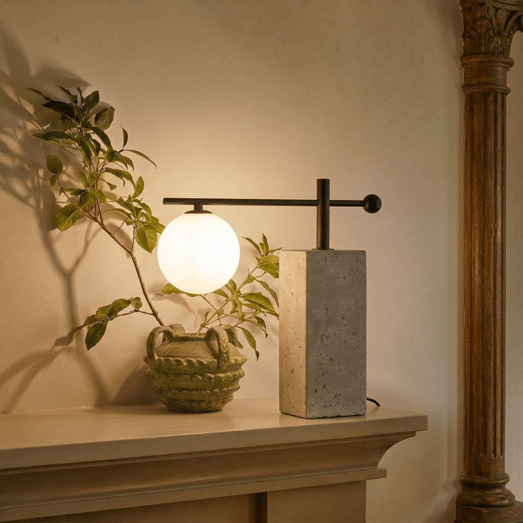 This Clérachic table lamp glows warmly on a mantel beside a leafy branch in a carved ceramic vase.