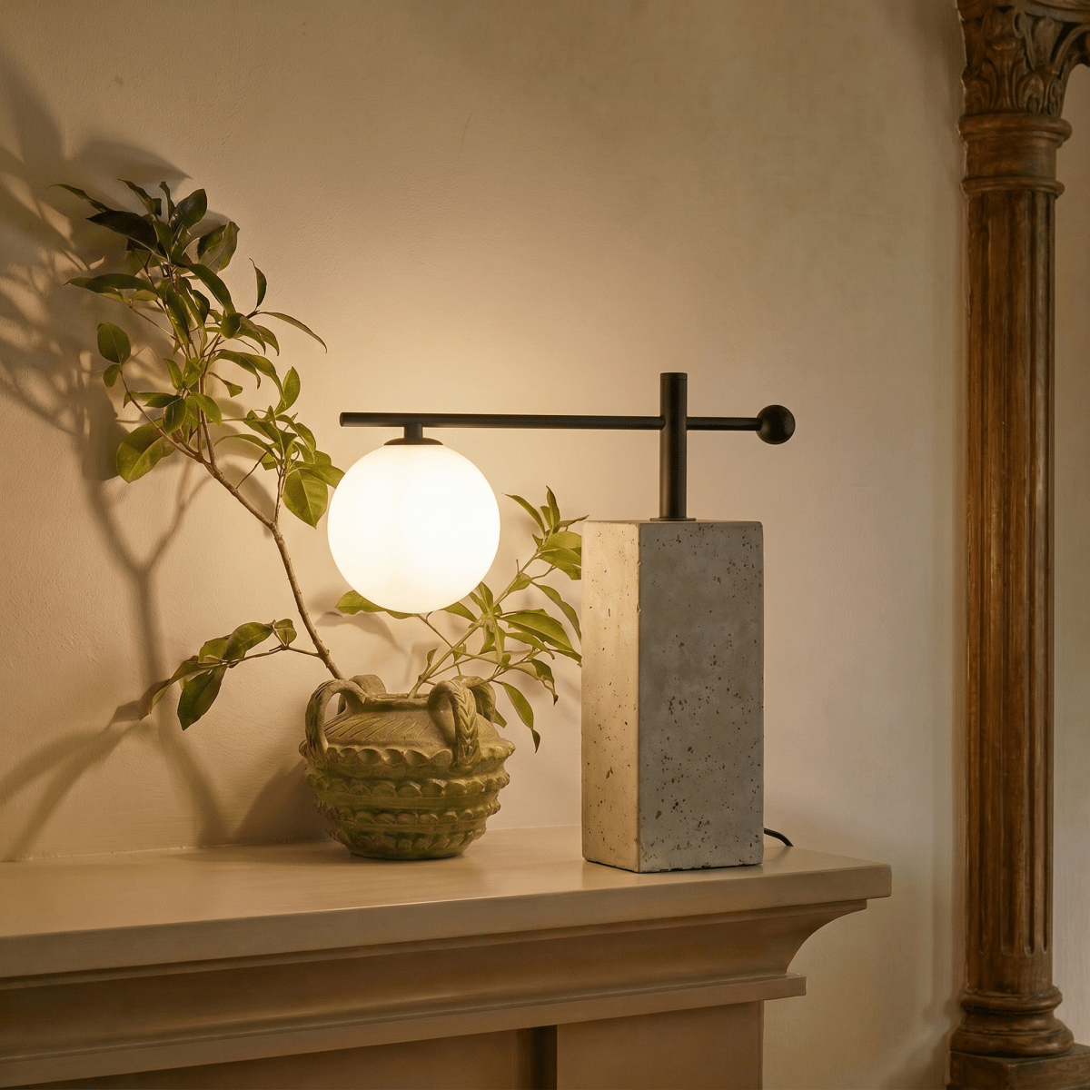 This Clérachic table lamp glows warmly on a mantel beside a leafy branch in a carved ceramic vase.
