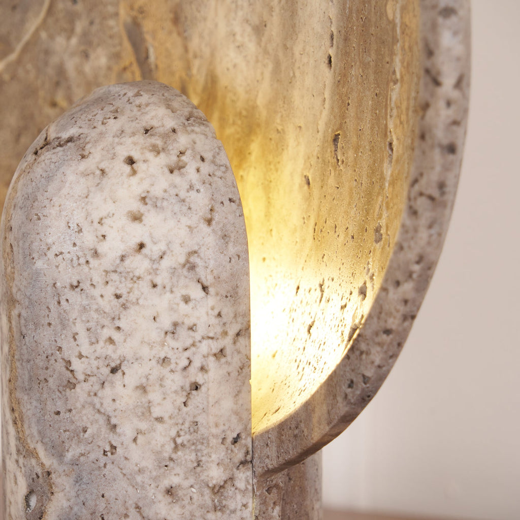 Close view of the pitted travertine stem and the warm light spilling across the inner face of the disc on this Clérachic lamp.