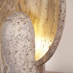 Close view of the pitted travertine stem and the warm light spilling across the inner face of the disc on this Clérachic lamp.