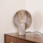 Angled view of this Clérachic lamp on a wooden cabinet, the veined disc leaning above a smooth rounded stem.