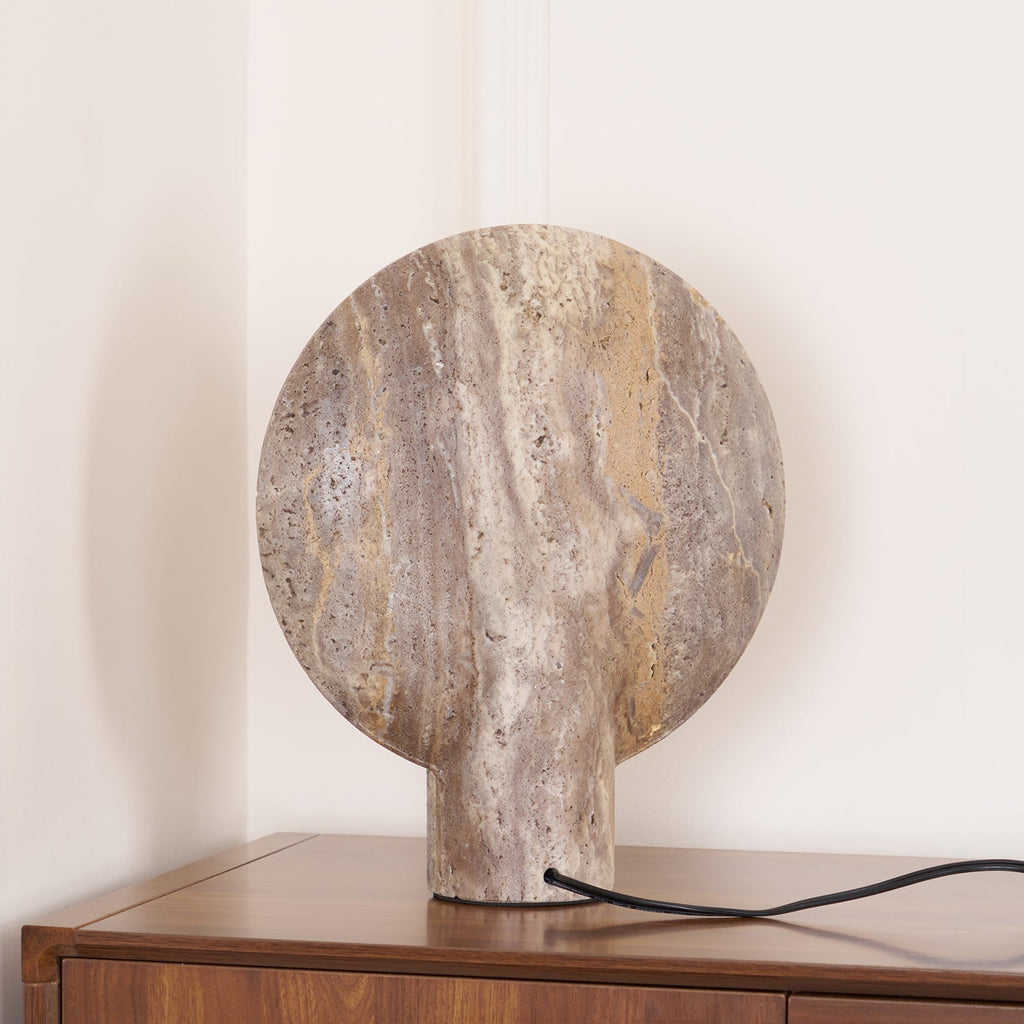 Rear view of the Clérachic travertine lamp on a walnut cabinet, showing the unlit back of the disc with its flowing brown veining.