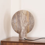 Rear view of the Clérachic travertine lamp on a walnut cabinet, showing the unlit back of the disc with its flowing brown veining.