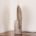 Side profile of this Clérachic lamp, the thin stone disc curving up behind the rounded travertine stem.