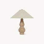 On a plain white backdrop, this Clérachic table lamp has a wide beige linen shade over a double-curved travertine base.
