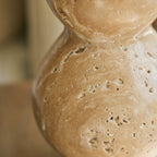 Close view of the pitted, honey-toned stone on the lower bulb of this Clérachic table lamp's base, with a soft blurred background.