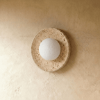 Clérachic round travertine wall light with a frosted white globe, switched off, showing the pitted natural stone dish.