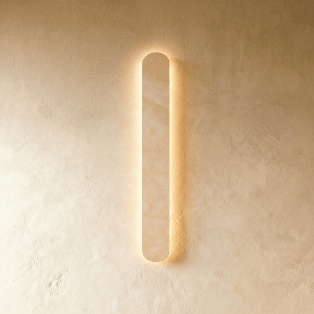 Clérachic slim cream travertine wall light with rounded ends, glowing softly behind the stone on a limewashed wall.