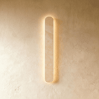Clérachic slim cream travertine wall light with rounded ends, glowing softly behind the stone on a limewashed wall.