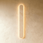 Clérachic taller cream travertine wall light, its rounded edge glowing warm against a textured plaster wall.