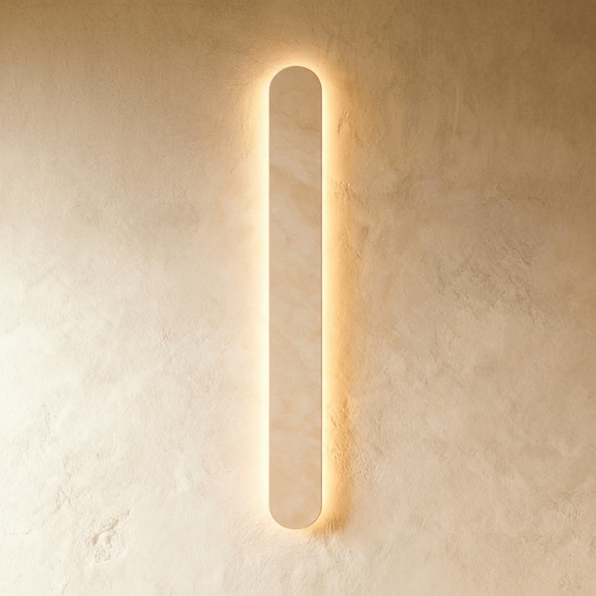 Clérachic taller cream travertine wall light, its rounded edge glowing warm against a textured plaster wall.