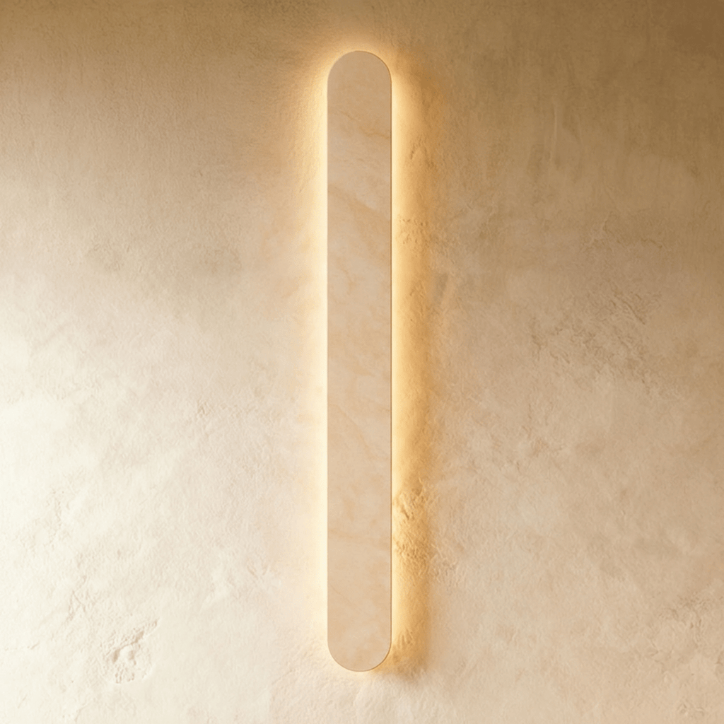 Clérachic tallest cream travertine wall light in the series, lit with a warm halo on a textured plaster wall.