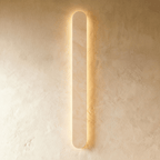 Clérachic tallest cream travertine wall light in the series, lit with a warm halo on a textured plaster wall.