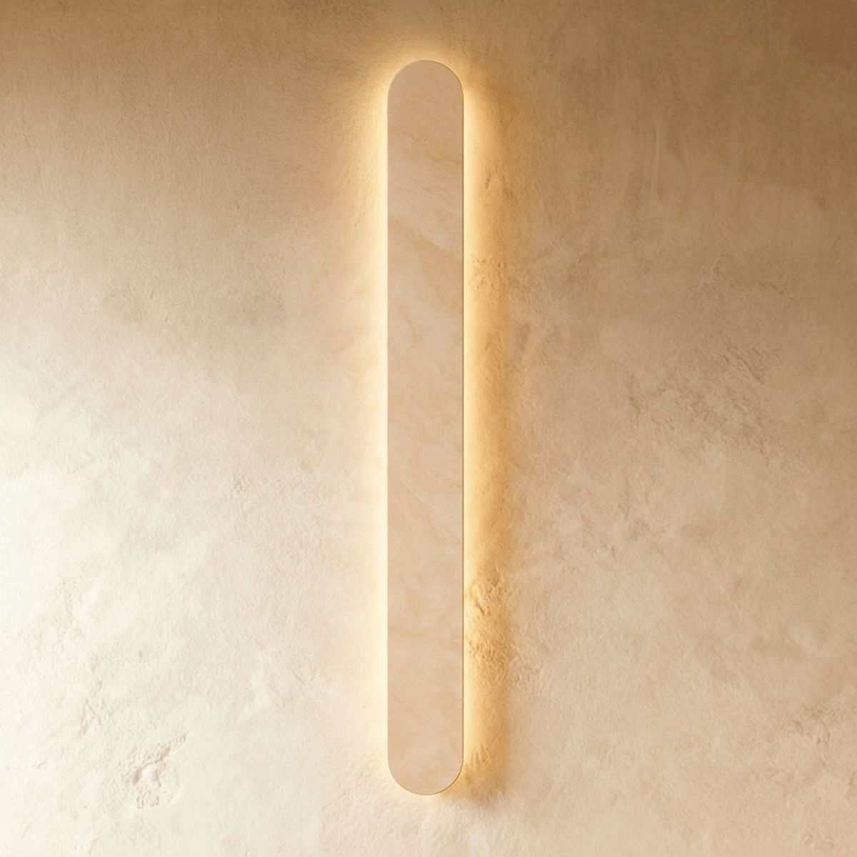 Clérachic tallest cream travertine wall light in the series, lit with a warm halo on a textured plaster wall.