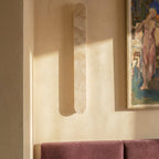 Clérachic travertine wall light with veined cream and soft-pink stone, shown in warm daylight near a framed painting.