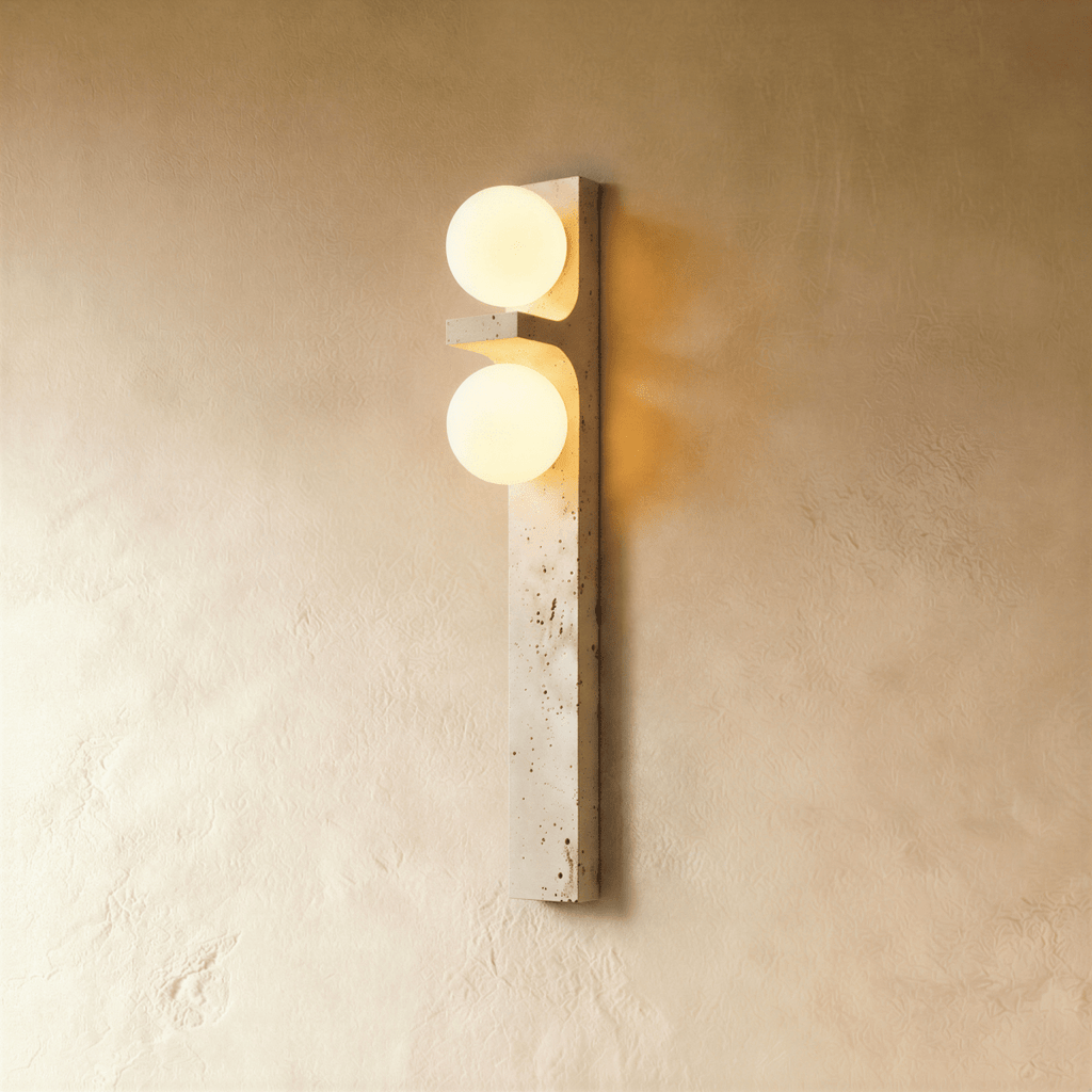 Clérachic vertical travertine wall lamp with two glowing frosted glass globes, mounted on a warm limewashed plaster wall.