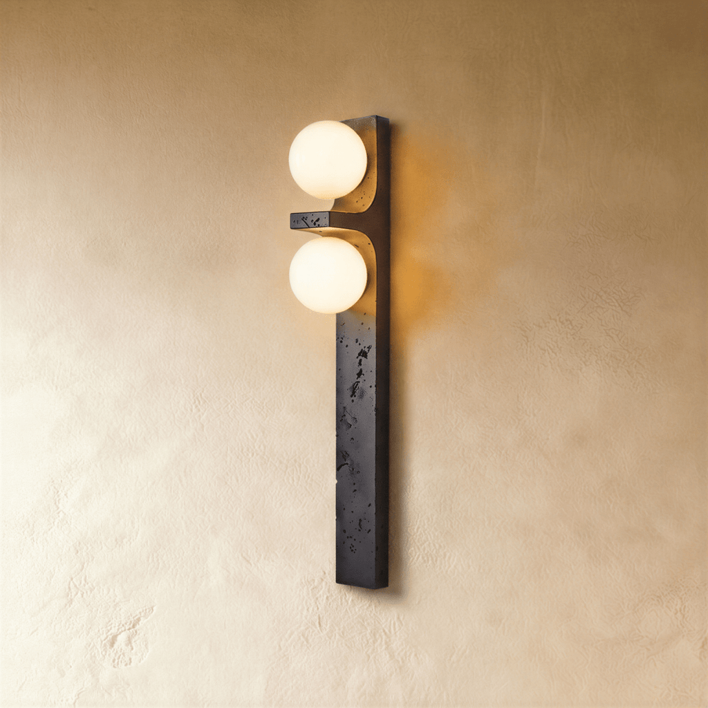 Clérachic vertical wall lamp in black stone-effect finish with two lit frosted glass globes on a warm plaster wall.