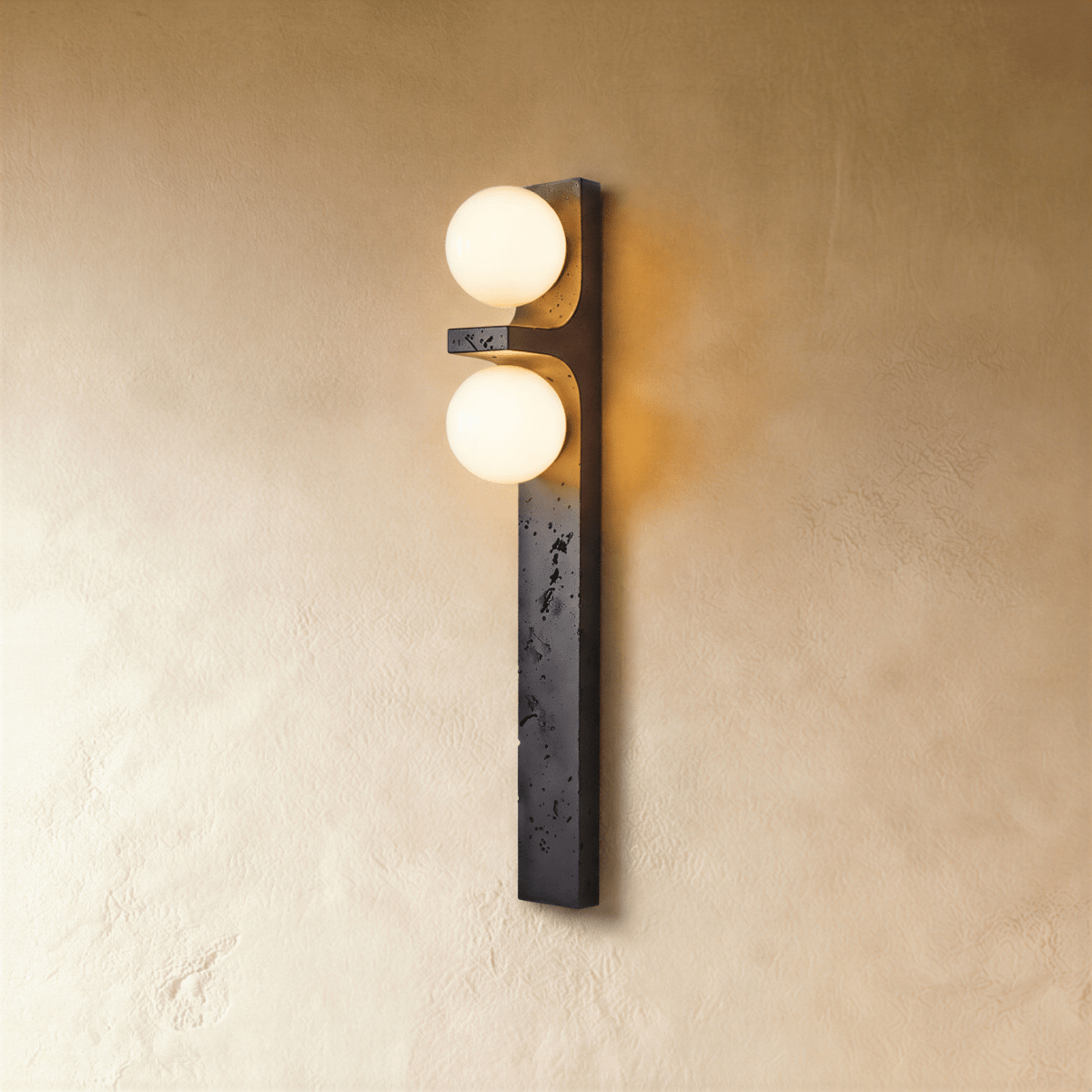 Clérachic vertical wall lamp in black stone-effect finish with two lit frosted glass globes on a warm plaster wall.