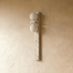 Clérachic travertine wall lamp switched off, showing two matt white glass globes and the pitted cream stone bar on plaster.