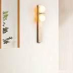 Clérachic travertine wall lamp with two glowing globes beside a tall mirror and a fluted panel in a bright, calm room.